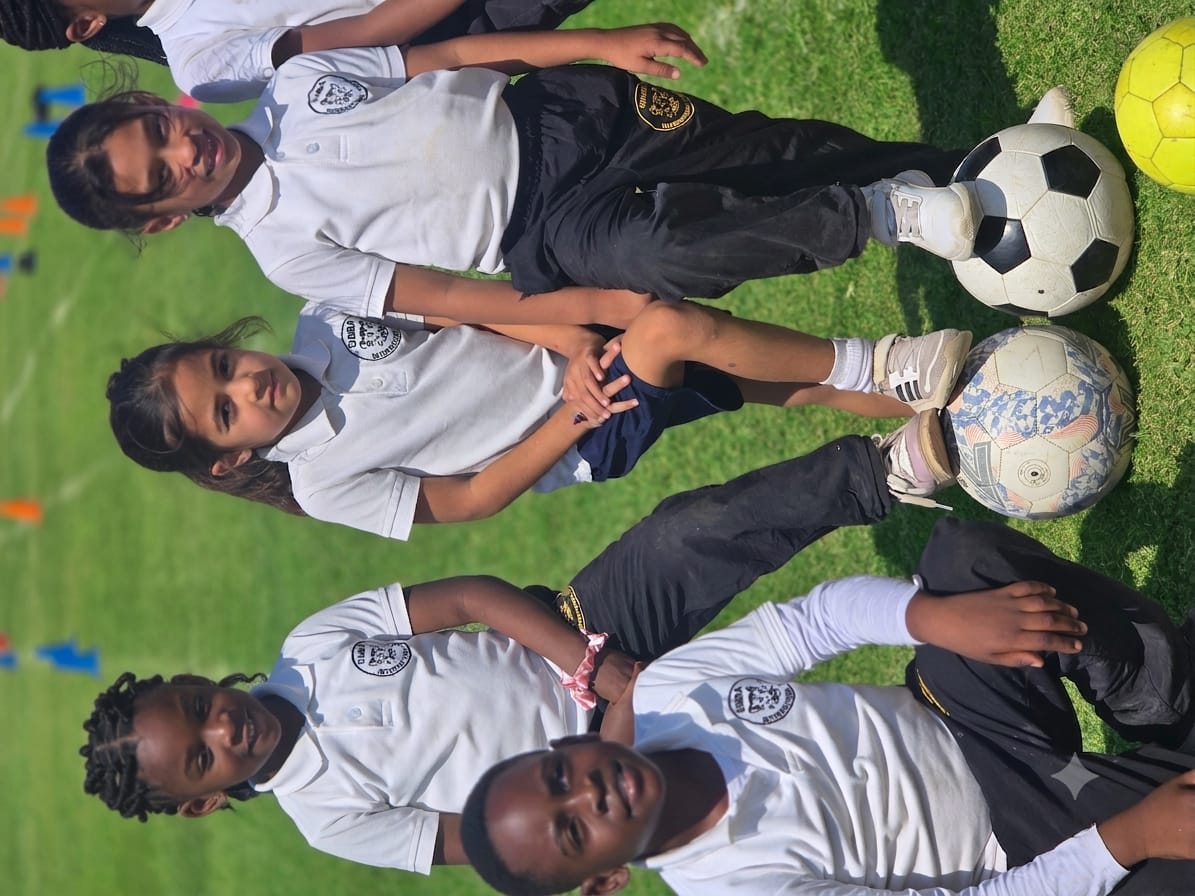 Primary pupils on the field at football practice, resting a foot on the ball between drills