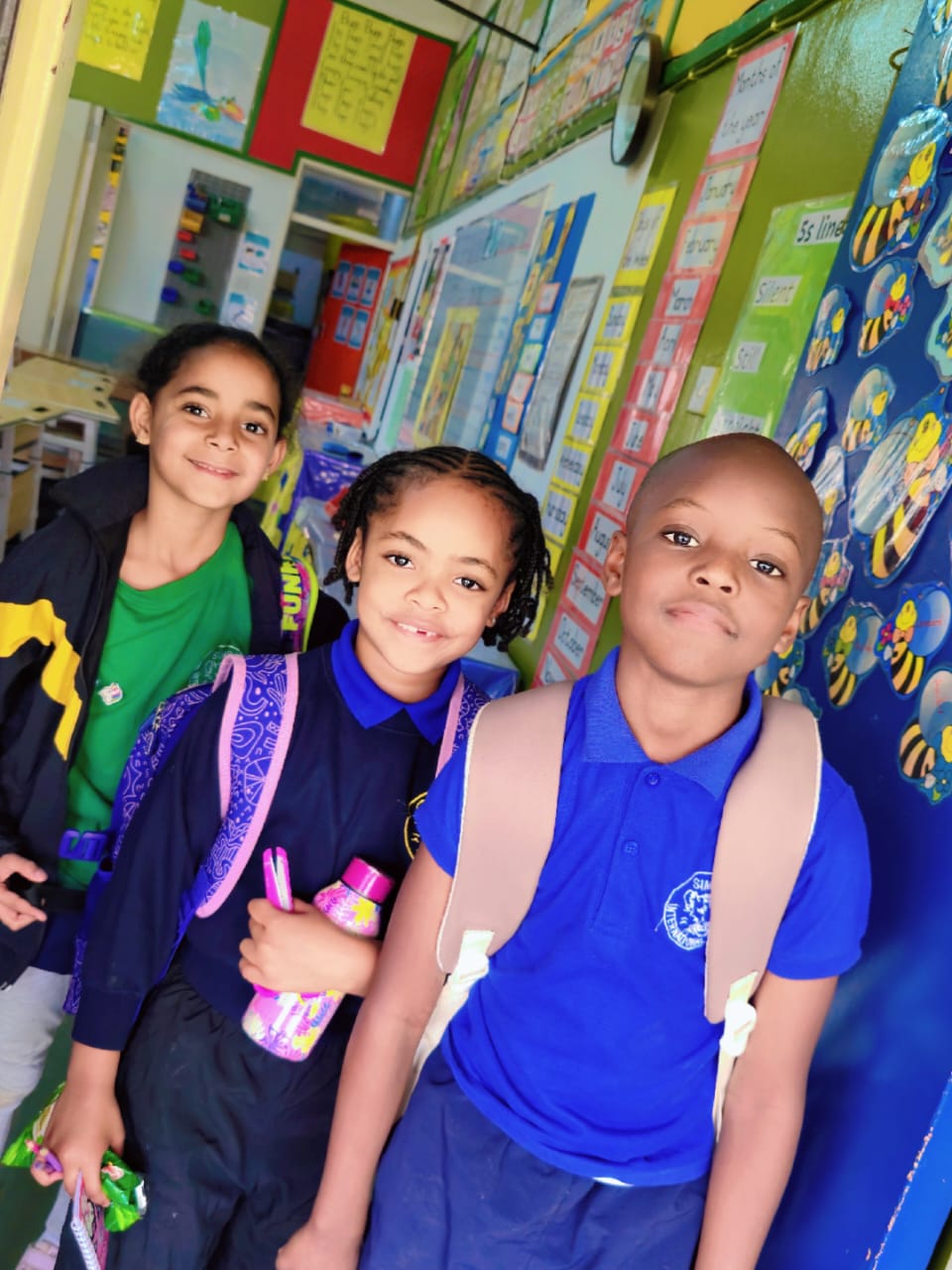 Three primary friends with their backpacks, ready for the walk home after school.